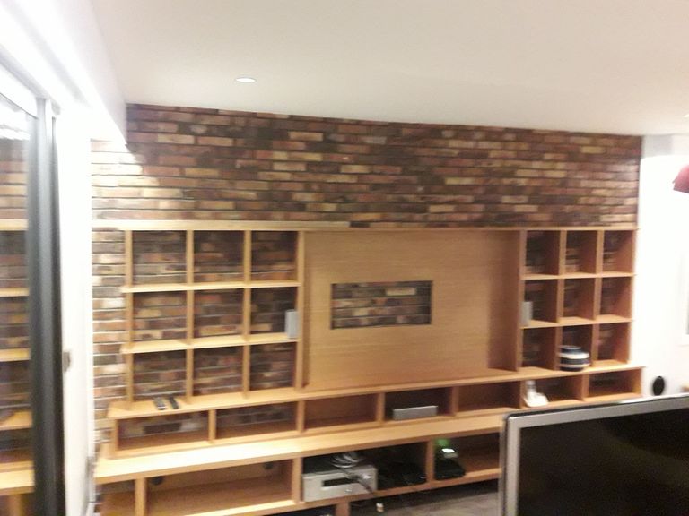 Bibliothèque sur mesure en bois clair posée devant un mur de brique