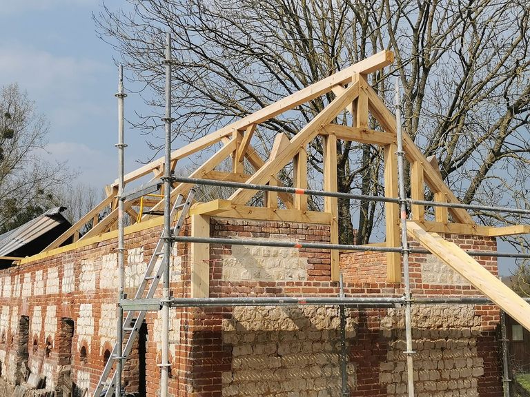 Ferme de charpente levée sur le pignon d’un bâtiment en brique et silex