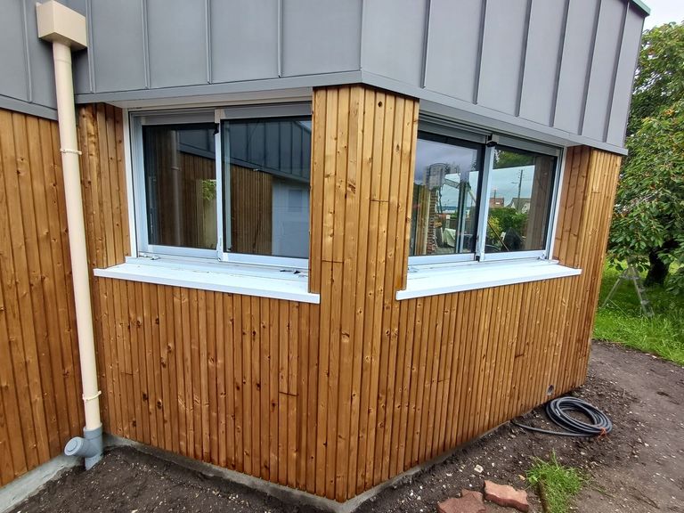 Angle d’une extension bardée de bois, fenêtres blanches et couverture en zinc