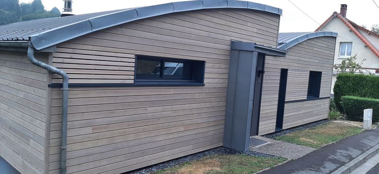 Extension à la façade courbe, bardée de lames grises