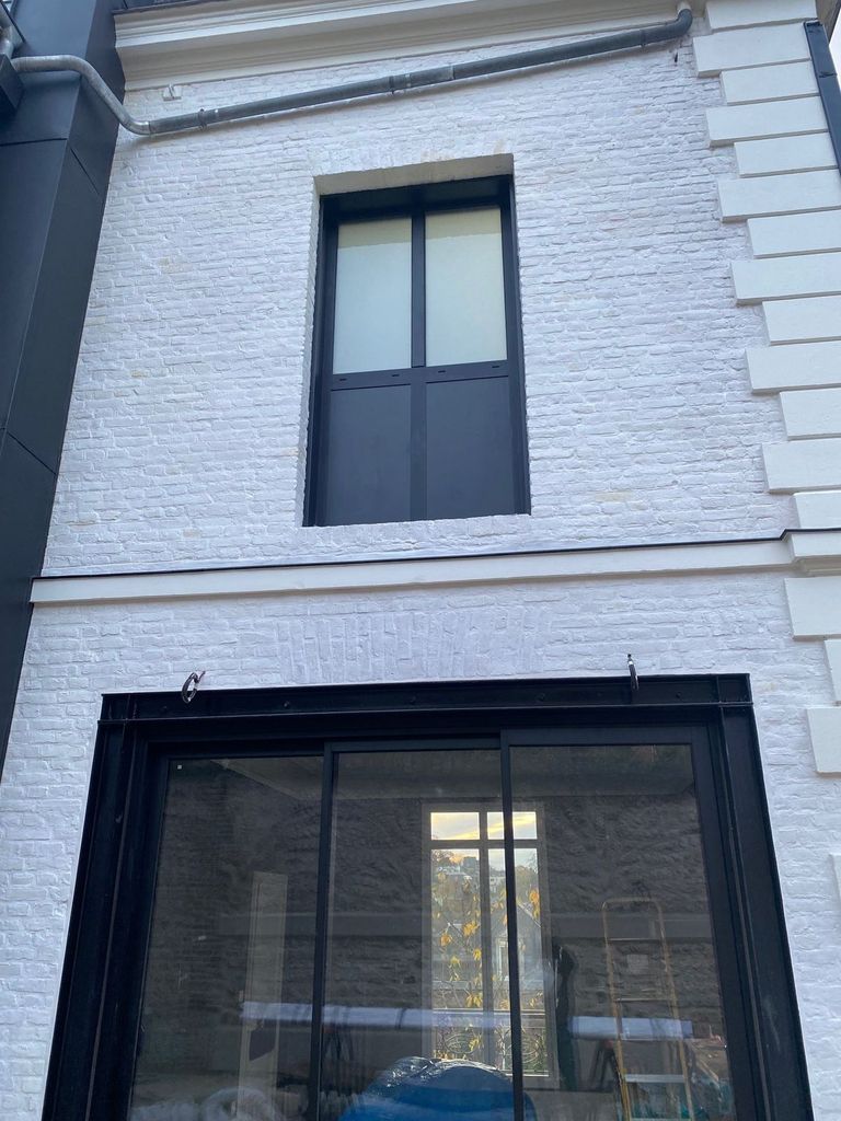 Fenêtre à châssis noir posée dans une façade en brique peinte en blanc
