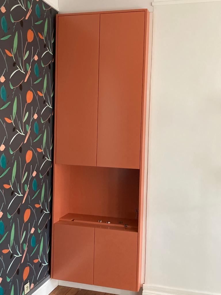 Placard sur mesure laqué corail avec niche ouverte, contre un papier peint à motifs