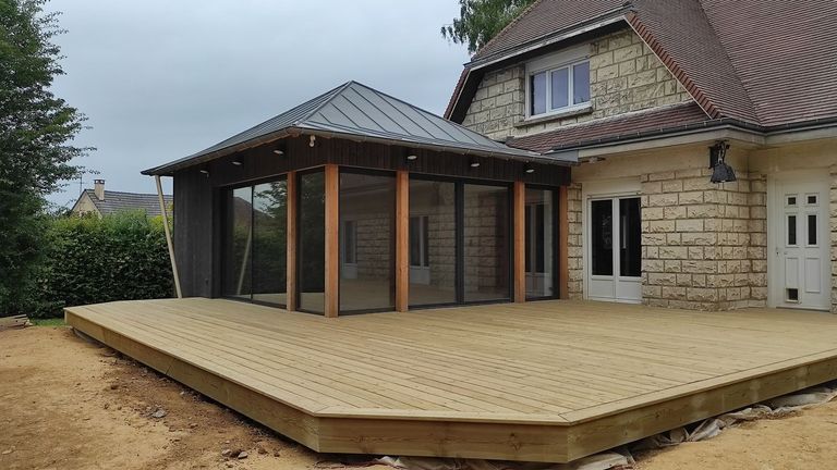 Terrasse en bois construite autour d’une extension vitrée