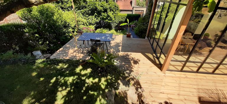 Terrasse en bois posée devant une véranda, dans un jardin planté